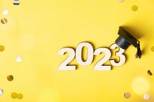 Class of 2023 concept. Wooden number 2023 with graduated cap on colored background with tinsel and bokeh photo