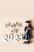 Class of 2023 concept. Wooden number 2023 with graduate statuette on beige background photo