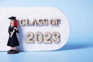 Class of 2023 concept. Wooden number 2023 with graduate statuette on color background photo