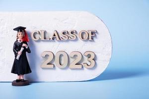 Class of 2023 concept. Wooden number 2023 with graduate statuette on color background photo