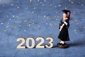 Class of 2023 concept. Wooden number 2023 with graduate statuette and fly festive tinsel photo