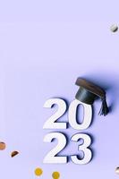 Wooden number 2023 with graduated cap and fly tinsel on purple background. Class of 2023 concept. photo