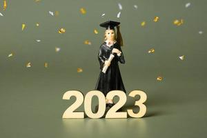 Class of 2023 concept. Wooden number 2023 with graduate statuette with festive tinsel photo
