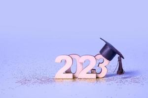 Class of 2023 concept. Wooden number 2023 with graduated cap on colored background photo