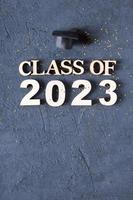 Class of 2023 concept. Wooden number 2023 with golden tinsel and graduated cap on dark background photo