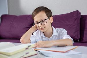 joven chico leyendo libro a hogar. educación, infancia, deberes y colegio concepto. foto