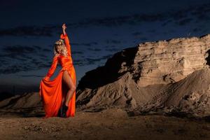 Woman in orange dress with slim naked legs posing near the sand hill photo