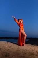 Young woman in orange dress posing at the background of blue sky photo