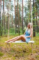 Young beautiful woman in short blue dress posing on a rope swing with bouquet of white flowers photo