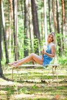Young beautiful woman in short blue dress posing on a rope swing with bouquet of white flowers photo