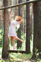 Blond young woman with slender naked legs in short dress and straw hat posing on a rope swing photo