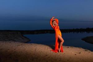 Young woman in orange dress posing at the background of blue sky photo