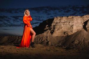 Woman in orange dress with slim naked legs posing near the sand hill photo