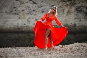 Beautiful woman in orange dress posing at the background of sand hill photo