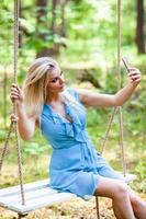 Beautiful blond woman in blue dress using smartphone to taking selfie photo