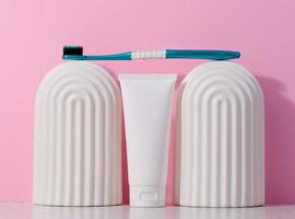 White plastic toothpaste tube and toothbrush on a pink background. photo