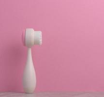 White plastic face scrub brush on a pink background, cosmetic tool photo