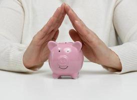 A ceramic piggy bank and female hands above it, a concept of saving money photo