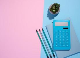 Blue notepad, calculator and wooden pencil on a blue background, top view photo