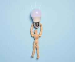 A wooden mannequin holds a glass lamp against a blue background, representing the concept of searching for new ideas and optimal solutions photo