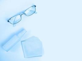Glasses care product. Glasses, spray, napkin for glasses on light background. Blue monochrome background. Ophthalmology photo