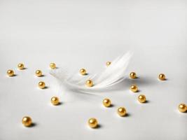 Beautiful white feather and gold beads on a light background. Blurry image. photo