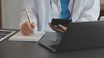 médico trabajando con ordenador portátil computadora y escritura en papeleo. hospital antecedentes. video