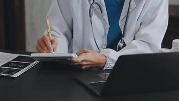 Arzt Arbeiten mit Laptop Computer und Schreiben auf Papierkram. Krankenhaus Hintergrund. video