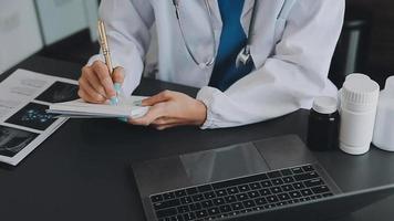 médico trabajando con ordenador portátil computadora y escritura en papeleo. hospital antecedentes. video