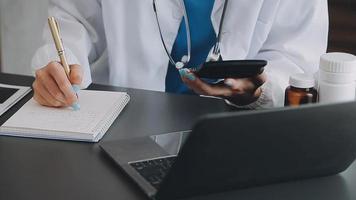 Doctor working with laptop computer and writing on paperwork. Hospital background. video