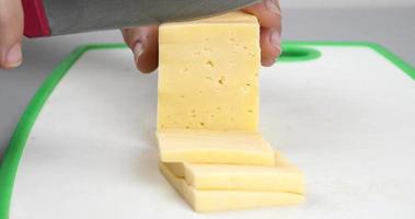 cutting cheese into slice pieces with a knife closeup video