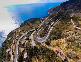 aerial shot of cars passing through a spiral road surrounded by trees in the countryside photo