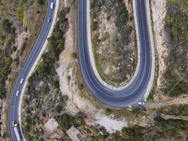 aerial shot of cars passing through a spiral road surrounded by trees in the countryside photo