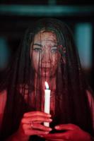 an Asian woman with a transparent veil covered in blood holds a candle in her hand while performing a ritual photo