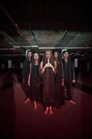 a group of devil worshipers in all black clothes and transparent veils holding candles together during a worship ritual in a building photo