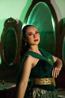 a entertainer woman with a green dress and scarf posing very beautiful and exotic in front of a makeup mirror in a green room photo