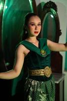 un indonesio hembra bailarín en un verde disfraz bailes en frente de un vendaje mesa muy hermosamente y graciosamente foto