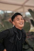 an Asian man in a black denim jacket posing with a cheerful face and very handsome in a cafe photo