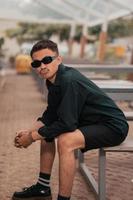 an Asian man with a mustache face wearing a shirt and sunglasses while hanging out with his friends in a cafe photo