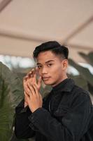 an Asian man in a black denim jacket posing with a cheerful face and very handsome in a cafe photo