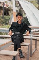 an Asian teenager in a black denim jacket posing by sitting on a cafe chair and relaxing photo