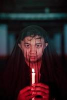 an Asian man with a transparent hood covered in blood holds a candle in his hand with a very scary expression photo