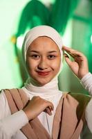 a Muslim woman in a white headscarf and white clothes poses with her hands without the slightest makeup on her face and smiles during a photo shoot