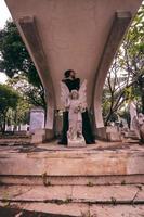 a young witch in a black dress is standing between the tombstones shaped like an angel while visiting the cemetery photo