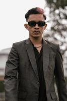 an Asian man with sunglasses posing in a gray suit in the yard photo