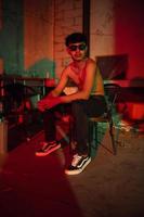 a gay man in sunglasses and denim pants sits relaxing in a club to celebrate photo