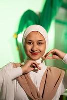 a Muslim woman in a white headscarf and white clothes poses with her hands without the slightest makeup on her face and smiles during a photo shoot