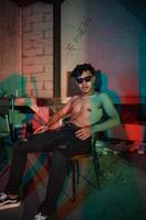 a gay man in sunglasses and denim pants sits relaxing in a club to celebrate photo