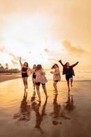 un grupo de asiático adolescentes en camisas corriendo con su amigos con muy alegre expresiones en el playa foto