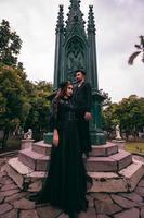 un par de asiático adolescentes en pie en frente de el funeral Monumento y frente a cada otro con todas negro ropa y de miedo expresiones foto